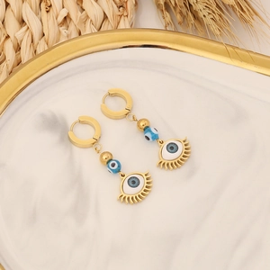 Close-up of golden evil eye earrings on marble tray with natural wheat decoration
