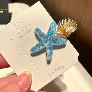 Detail of starfish hair clip with blue sequins, pearls and a golden shell element