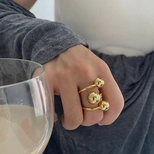 Three gold spheres on a multi-layer brass ring worn on finger while holding a glass