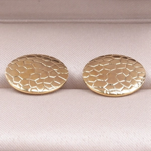 Detail of round gold geometric earrings with honeycomb texture on satin display box