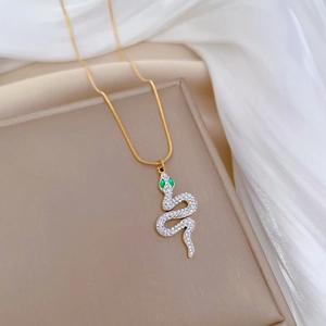 Detail of snake pendant with green gem eyes and pavé white crystals on a gold chain