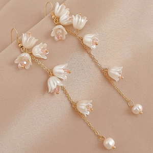 Détail de boucles d'oreilles muguet avec fleurs blanches, perles roses et chaînes dorées