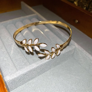 Close-up of golden leaf open bangle with white enamel inlay on a velvet jewelry display