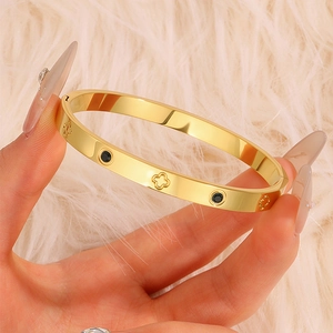 Detail of gold titanium clover bracelet with black zircon inlay held against plush background