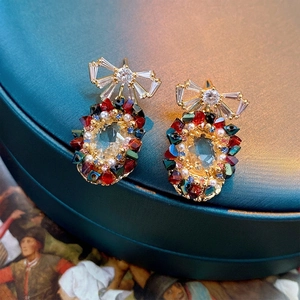 Elegant gold bow earrings with colorful gemstones and pearls on a velvet jewelry box