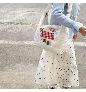 Detail of white quilted tote bag featuring red house and puppy embroidery with text