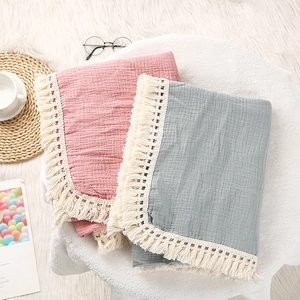 Detail of pink and grey folded soft cotton baby blankets with tassel edges on a white rug