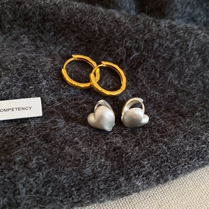 Close-up of textured gold hoops and matte silver heart earrings on grey fabric background