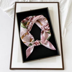 Detail of pink floral satin scarf tied inside a black gift box on a white fabric background