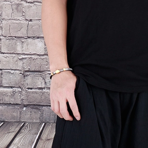 Detailed close-up of a layered black woven cord bracelet with metallic chain and gold accents