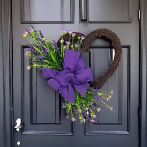 Detail of a heart-shaped vine wreath with purple flowers and a large silk bow on a door