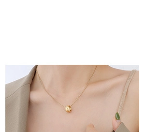 Close-up of minimalist golden cylinder pendant on a fine chain worn with a beige blazer