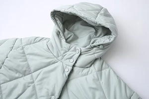 Detail of hooded quilted jacket featuring diamond stitching and press stud closure