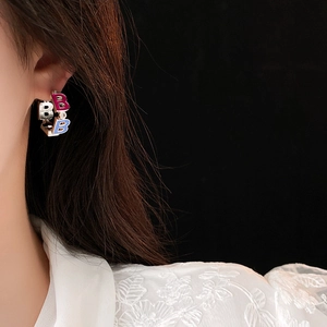 Close-up of a model wearing C-shaped gold hoop earrings with colorful enamel B letters