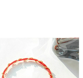 Close-up of minimalist red braided string bracelet with gold metallic bead details