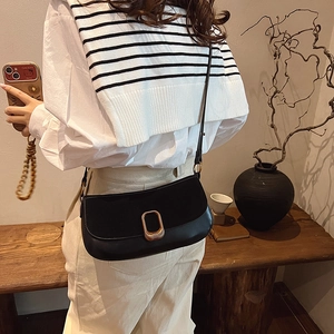 Classic black leather shoulder bag with gold metal buckle shown on model in a cozy setting