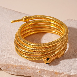 Gold snake wrap bracelet with black gemstone eyes on minimalist stone display