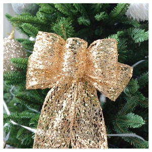 Close-up of a large gold sequined Christmas tree bow topper hanging on green branches