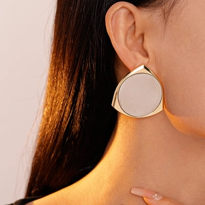 Close-up of elegant triangular gold earrings with beige inlay worn by a model