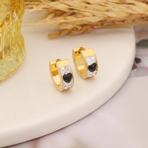 Detail of gold huggie hoop earrings with black heart stones and white enamel details