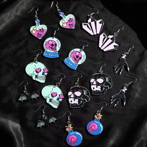 Gothic Halloween earrings featuring skull, bat wings and pink heart icons on black satin