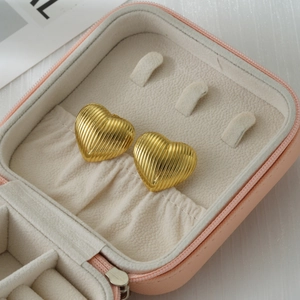 Detail of 18k gold heart stud earrings with vertical texture in a pink jewelry box