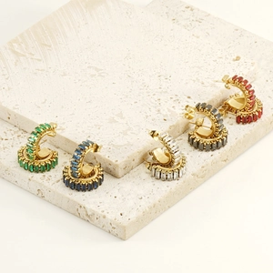 Detailed view of C-shaped earrings set with colorful rectangular zircons on stone background