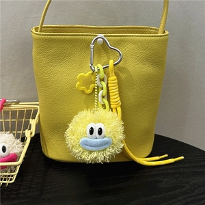 Close-up of a yellow leather bucket bag with a cute cartoon plush charm and heart clip