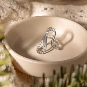 Detail of silver wavy layered open ring displayed in a ceramic bowl with textured fabric
