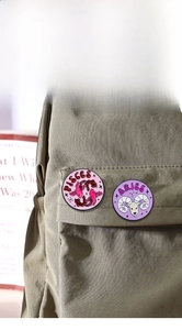 Detail of zodiac enamel pins showing Pisces and Aries designs on a green canvas backpack
