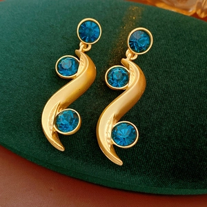 Macro shot of gold-plated S-shape earrings with three blue crystals on green velvet