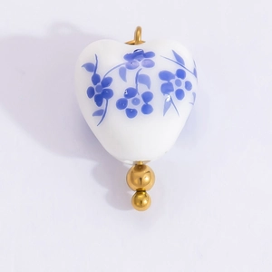 Detail of heart-shaped ceramic pendant with blue floral pattern and gold bead accents