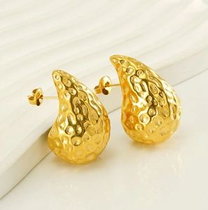 Macro shot of 18K gold teardrop earrings with hand-hammered texture on white stone