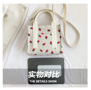 Detail view of corduroy tote bag with strawberry print and adjustable strap next to a tablet