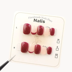 Handmade burgundy and white French manicured nails with diamond accents on display