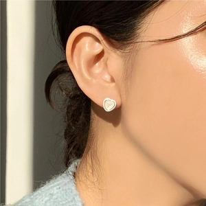 Close-up of heart-shaped mother of pearl stud earring with silver beaded edge on model