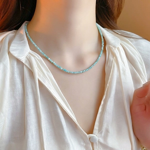 Close-up of a blue bead necklace worn by a model in a minimalist white shirt