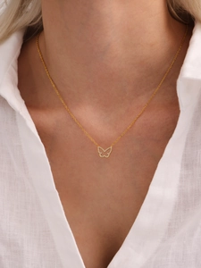 Close-up of a gold butterfly necklace with zircon stones worn by a model in a white shirt