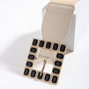 Close-up of beige elastic belt featuring a gold square buckle with black rhinestones