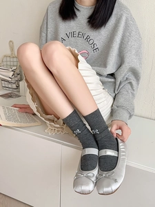 Detail of dark grey crew socks with ribbon bow paired with silver ballet flats