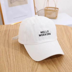 White baseball cap with Hello Weekend embroidery on wooden desk with home decor