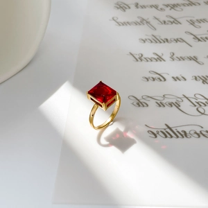 Detail of 18K gold titanium ring with a square-cut red zircon on artistic letter background