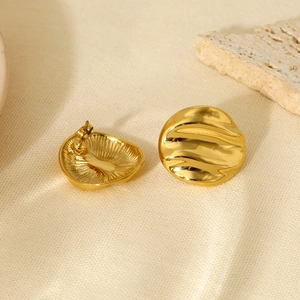 Irregular wavy gold disc stud earrings made of 316L stainless steel on natural linen