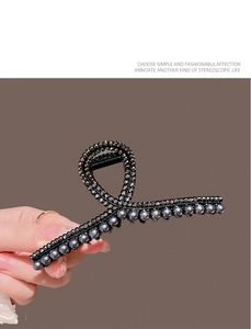 Detail of a black twisted hair claw clip with dark beads held against a brown backdrop