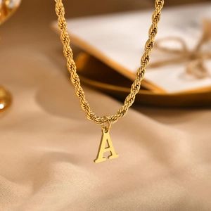 Detail of golden stainless steel twist chain necklace with letter A pendant on silk
