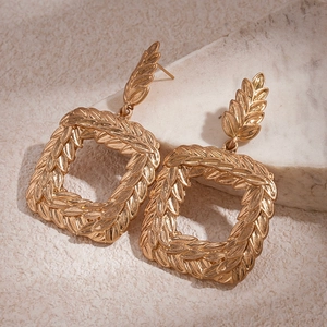 Detailed close-up of golden geometric square earrings with wheat ear relief textures
