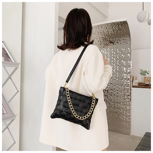Detail of a black woven crossbody bag with chunky gold chain on a model in a coat