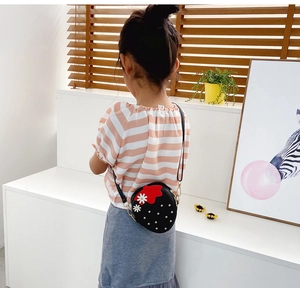 Detail of child wearing a round black crossbody bag with strawberry and daisy accents