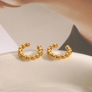 Close-up of golden beaded stainless steel ear cuffs on a white ceramic surface