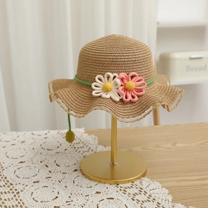 Close-up of children's woven straw hat with pink flowers on a gold display stand